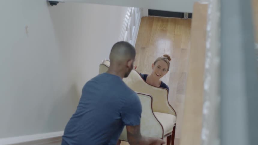Man and woman smiling and talking while carrying chair up stairs