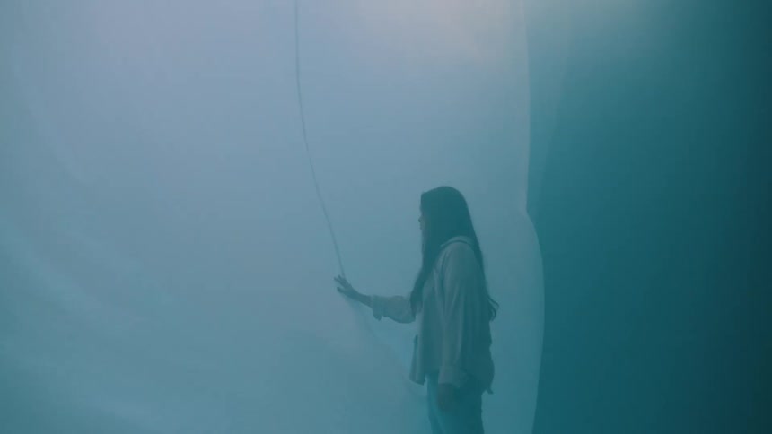 Woman reaching out to touch white hanging fabric while white fabric on the floor billows up
