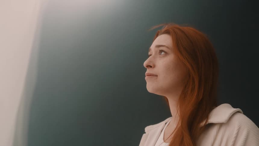 A woman gazes upward in quiet reflection against a soft minimal background