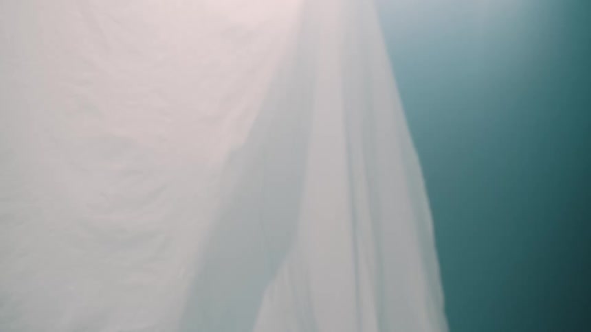A close up shot shows a large white fabric sheet rippling against a blue background