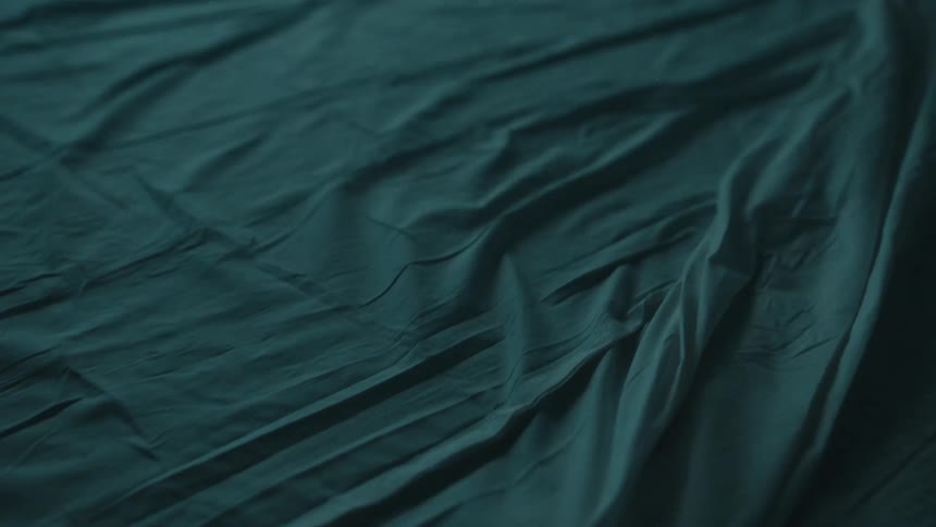 Green linen fabric is spread across the floor rumpled in soft folds as flickering light reflects off its surface