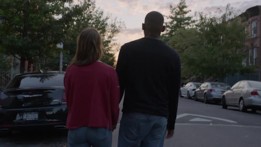 Woman and man, holding hands and walking along a city street at dusk