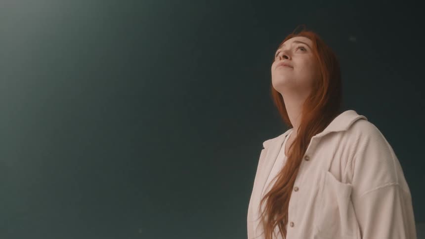 Woman wearing a lightcolored shirt looks upward against a dark background