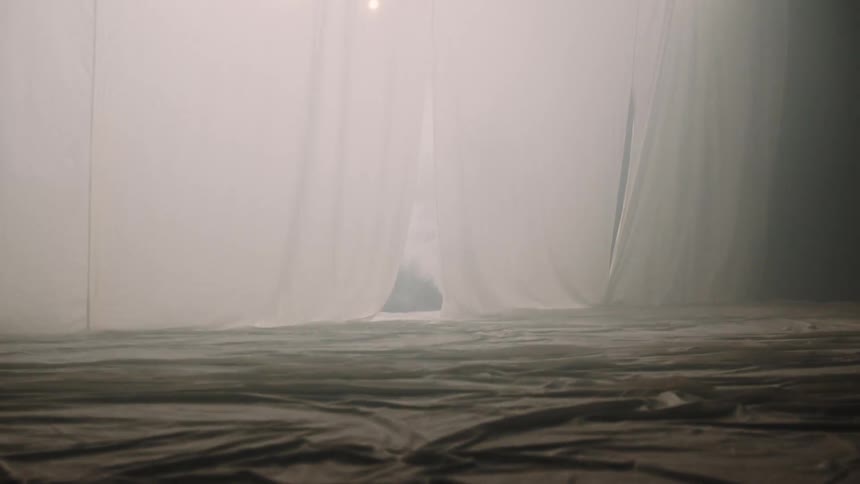 A low angle view shows a dark space with a large white fabric sheet illuminated by bright lights in the background