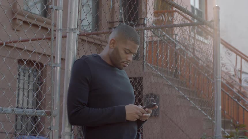 A man uses a phone by a fence