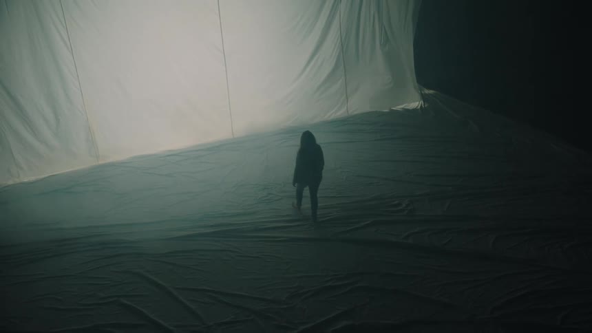 Person walking in a large space with suspended white fabric and diffused lighting