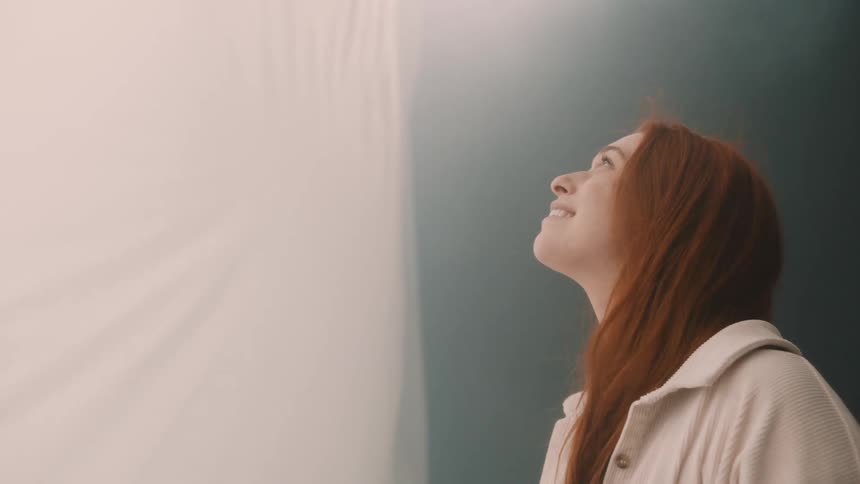 Woman looking upward beside a white curtain in an indoor setting