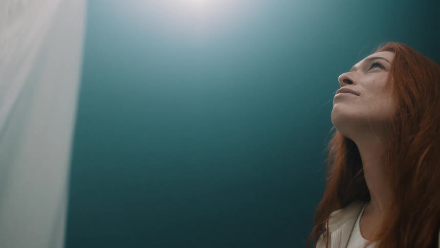 Woman looking upward in an indoor environment with soft lighting and fabric in the background