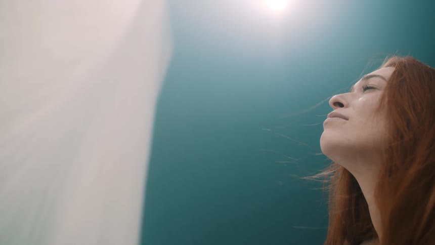 Young adult woman looking at a white curtain with a blue wall on the background indoors