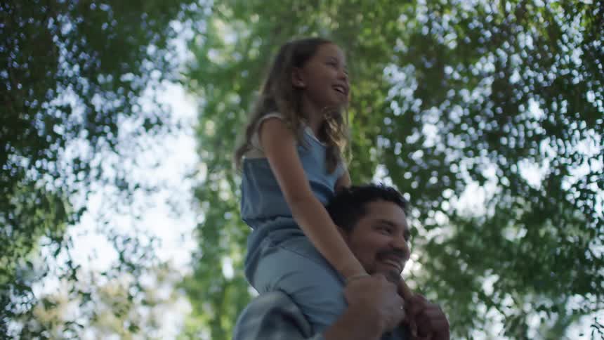 Daughter sits on her fathers shoulder with both laughing while walking in the woods