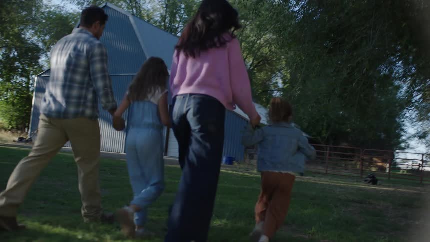 Family walks together on a rural farm toward a blue barn on a bright sunny day