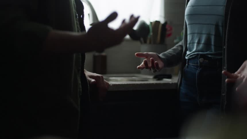 In a kitchen setting two people are shown from the waist down engaged in an animated expressive conversation using their hands after a few moments of gesturing back and forth one person turns and walks away leaving the other standing alone