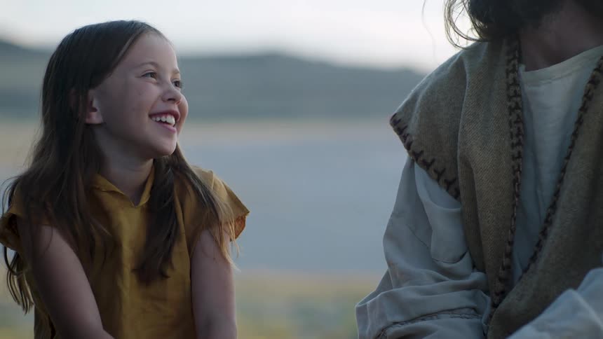 Child smiling outdoors beside an adult in a natural landscape