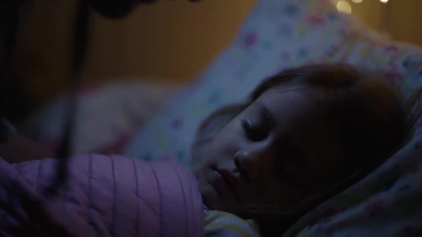 Father tucking his sleeping daughter in and kissing her