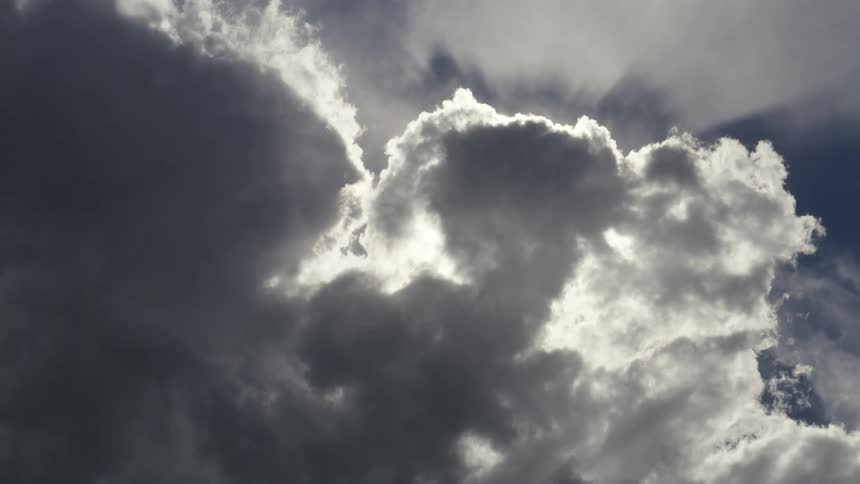 Sunlight streams from behind dense dark clouds creating a bright silver lining and dramatic rays in the sky the clouds shift slightly highlighting the contrast between the shadowed formations and the glowing light