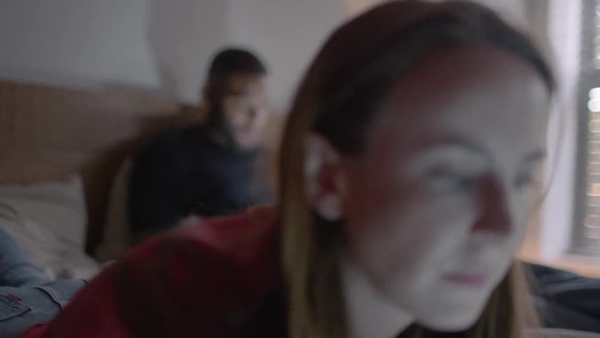 A man and woman use their devices in bed
