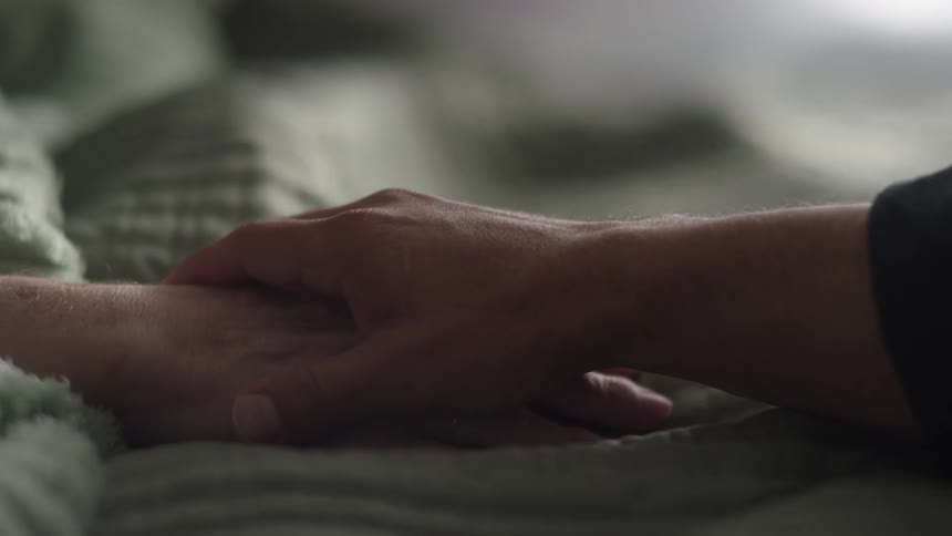 Hand gently holding another hand on a quilted fabric in an indoor setting