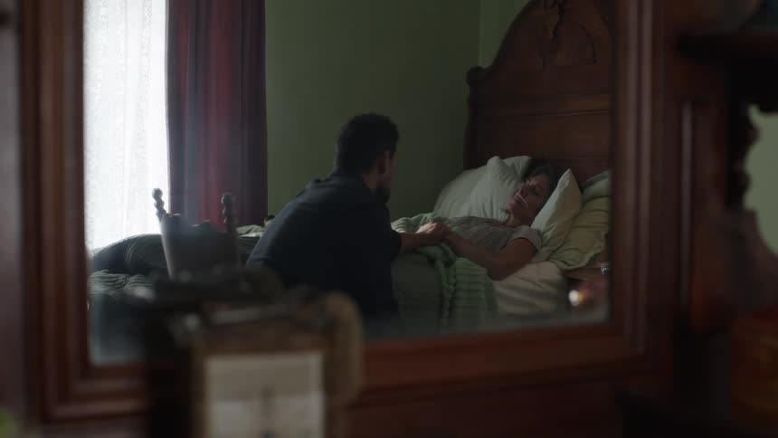 The mirror reflects the bed with a sick woman resting
