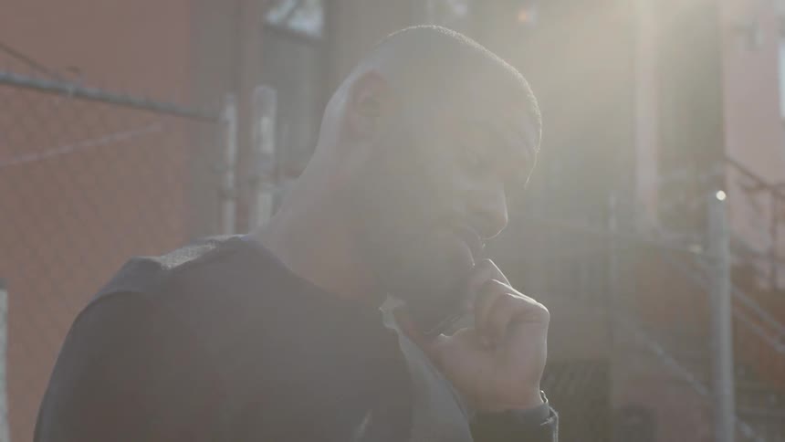 A man is talking outside on the phone by a fence
