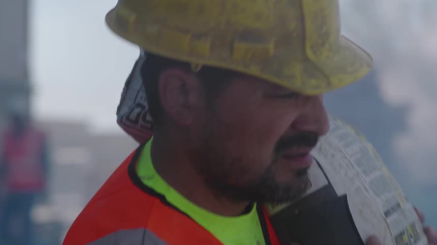 A latino construction worker carrying a cement bag at an industrial plant