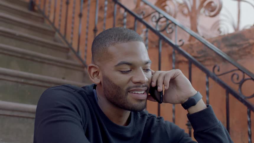 Man sits on stairs outside smiling as he talks on a cell phone