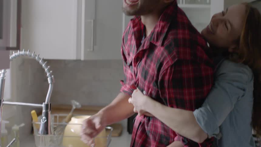 Woman hugging a man while he scrubs dishes