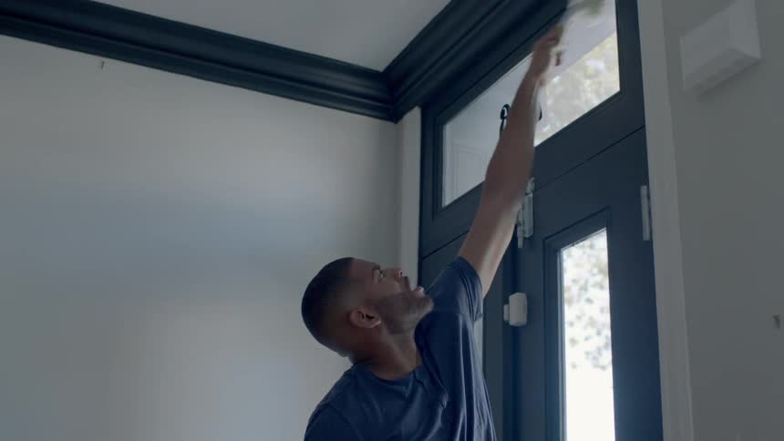 A man reaches up above a door frame to clean it