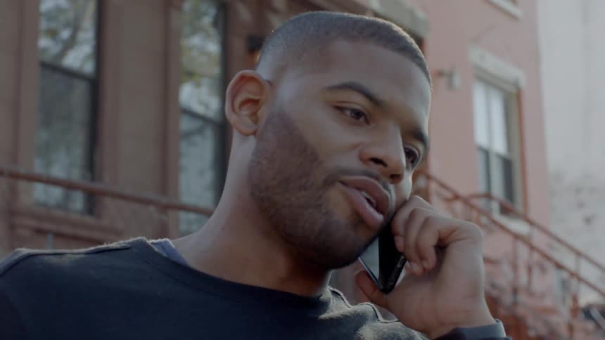 A man talks on a phone on a city sidewalk