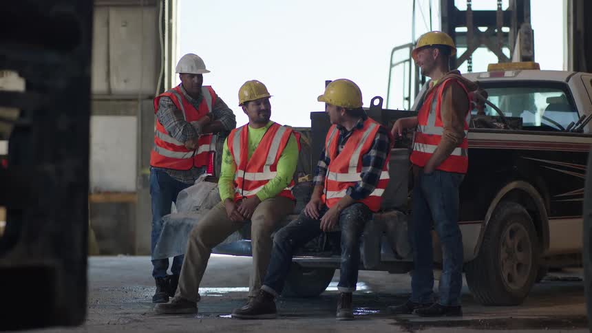 Group of construction workers talking beside a pickup truck in an industrial area