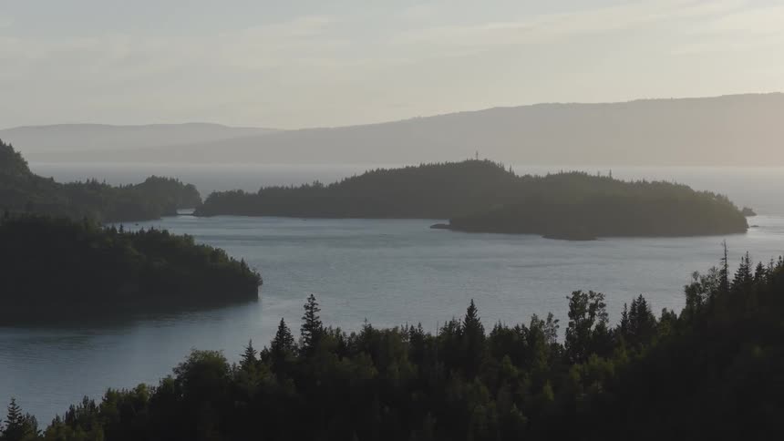 Forested islands surrounded by a lake with distant hills under soft light