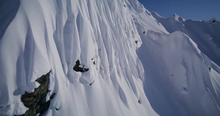 Steep snowcovered slope with rocky outcrops under a blue sky