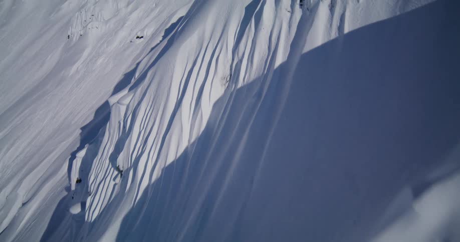 An aerial shot reveals the deep ridges and dramatic shadows of a steep snow covered mountain slope