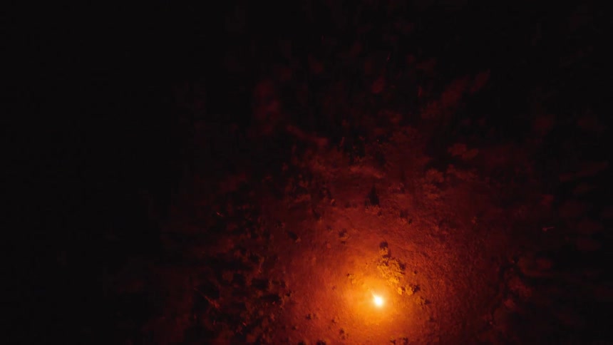Glowing blazing orb illuminates the snow as it moves through trees in the forest in the darkness