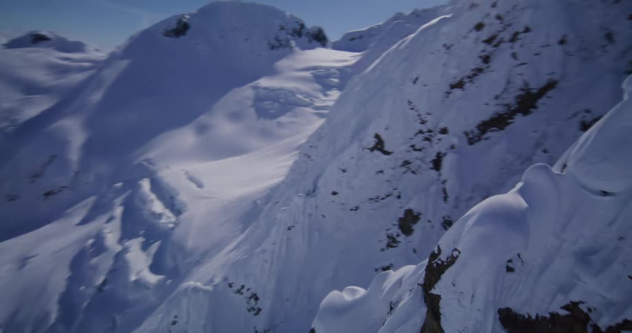 Snowcovered mountain range with sharp peaks and deep valleys under a blue sky