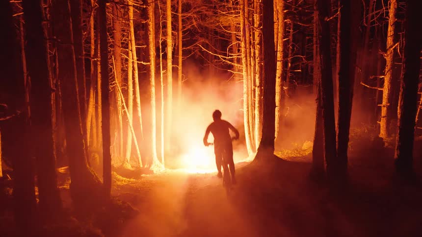 The man chases a fireball through the forest on his dirt bike