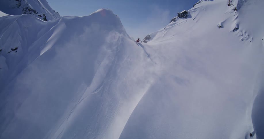 Helicopter flies over a snowcovered mountain slope under a high sun in the sky