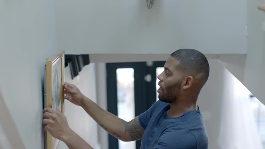 Man hangs picture on stairway wall