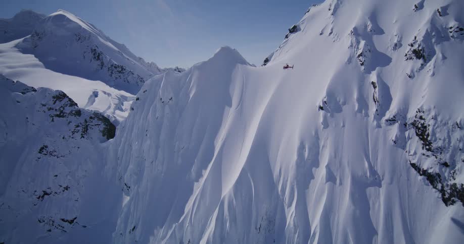 Helicopter flying over snow covered mountains cast a shadow on the slope