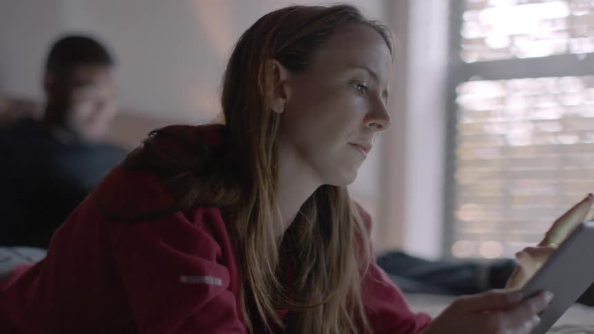 A man and woman use devices in a bedroom