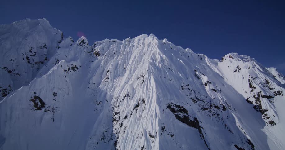 Steep mountain slopes covered in snow with exposed rocky ridges under a blue sky