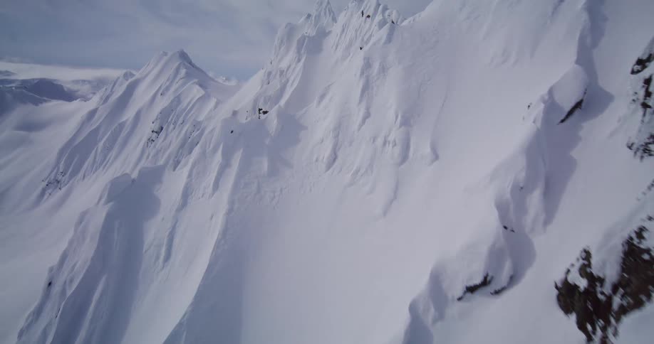 Heavy snow covers a steep ridge in mountainous terrain on a cloudy winter day