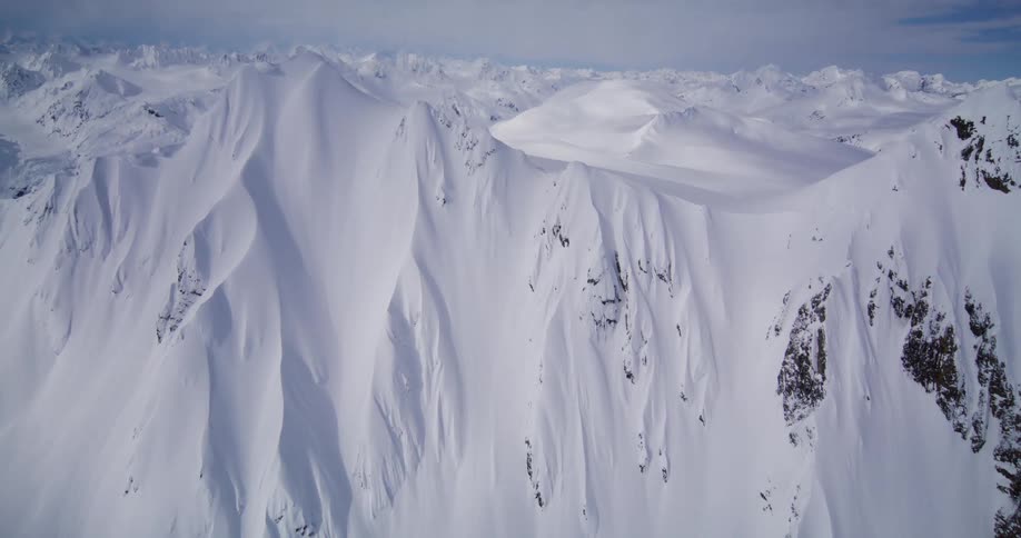 Snow covers a mountain with a steep side and a more gentle slope on a cloudy winter day