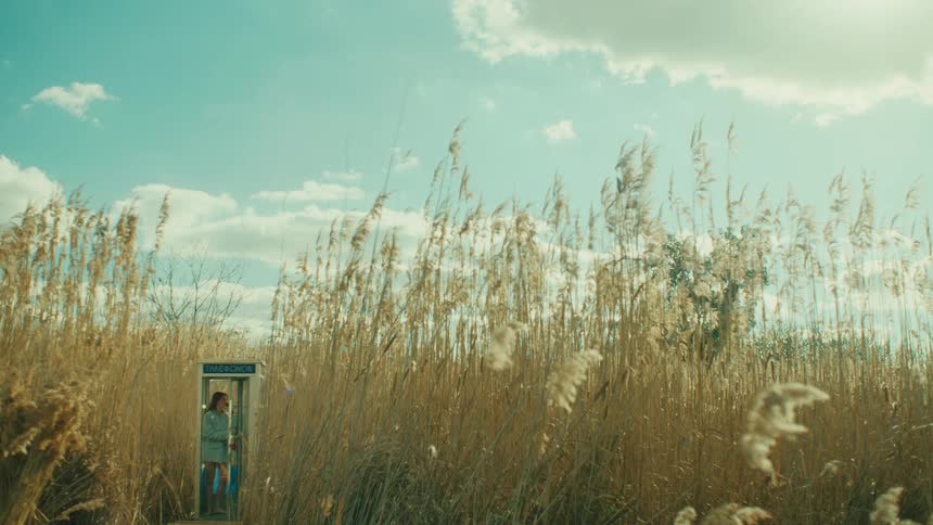 The woman is talking on the phone in the phone booth