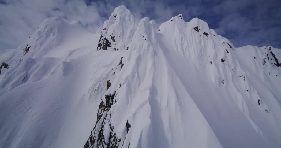 A mountain in the arctic stands covered in snow at midday its rough uneven slopes bright under the clear light