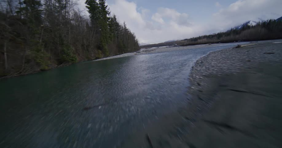 A fastmoving aerial shot glides low over a wide gravelbanked river winding through a snowy mountain valley