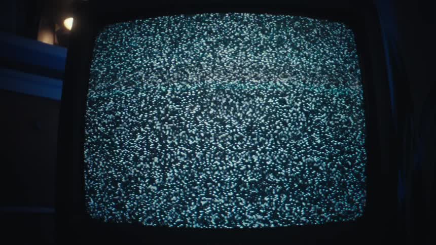 A medium shot shows a vintage television screen displaying flickering black and white static in a dimly lit room