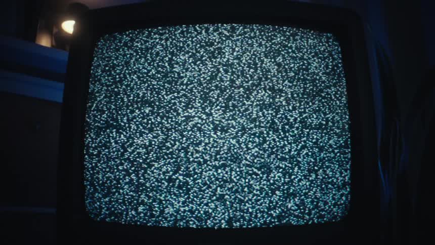 Television displays static noise in an indoor environment with bluetoned lighting and a lamp illuminated in the background