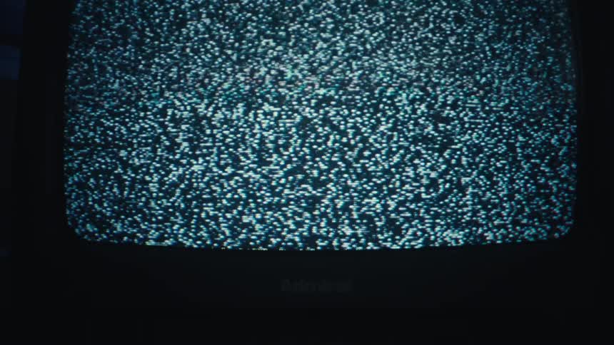A medium shot shows a vintage television screen displaying flickering black and white static in a dimly lit room