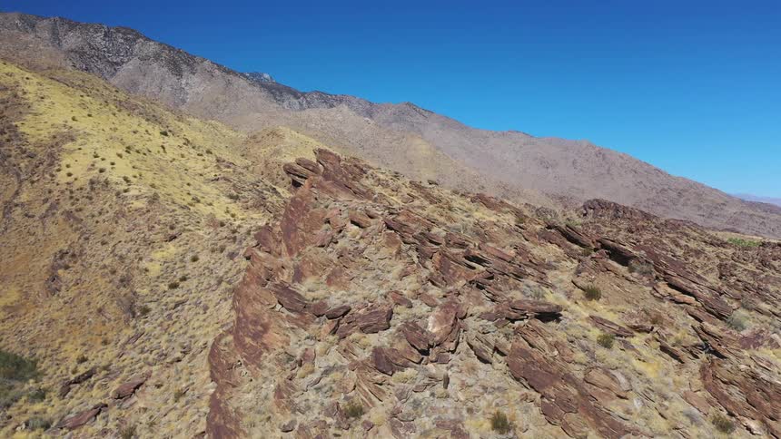Slanted rock formation in arid terrain with sparse vegetation under a clear sky