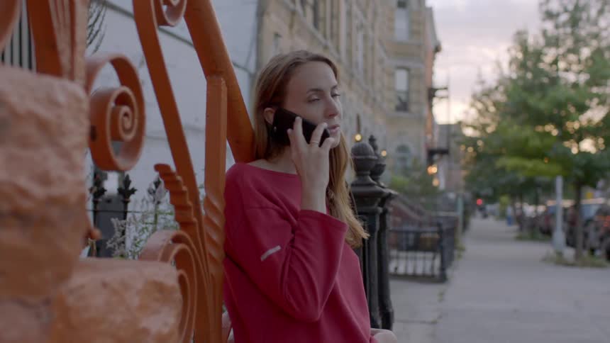 Woman leaning on a railing talks on a phone in a city
